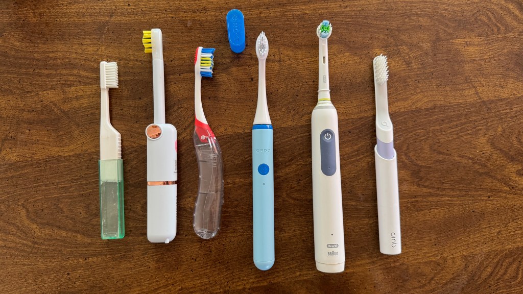 A variety of toothbrushes displayed on a wooden surface, including manual and electric toothbrushes in different designs and colors.