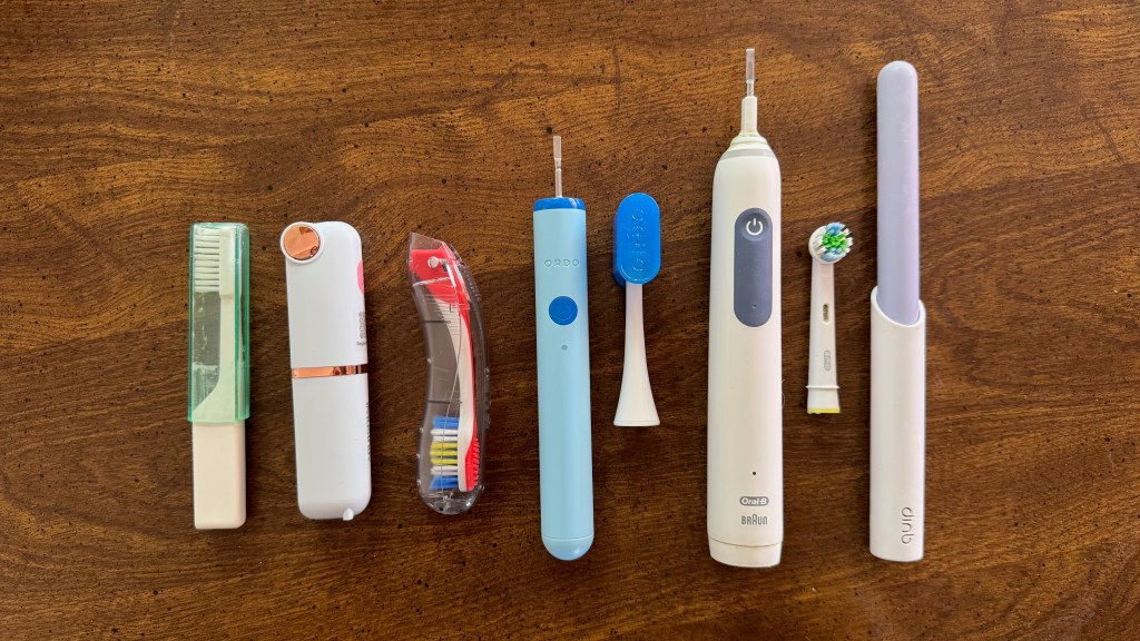 A collection of oral care tools arranged on a wooden surface, including toothbrushes, a toothbrush holder, and an electric toothbrush.